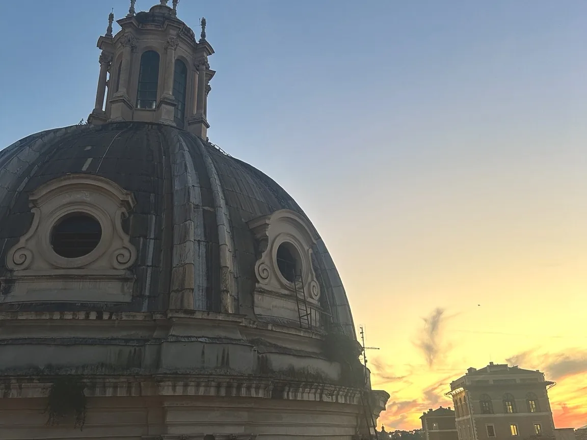 The dome of Santissimo Nome di Maria by Trajan's Forum against a golden-orange sunset, seen from the Oro Bistrot rooftop