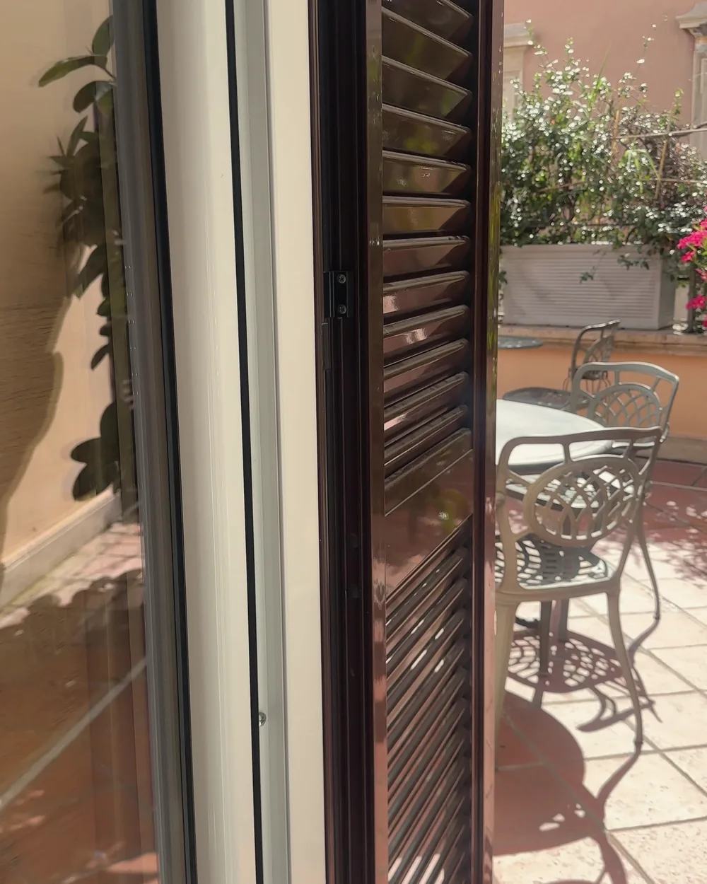 Tall wooden shutters and a glass door opening from the room onto a sunny terracotta terrace