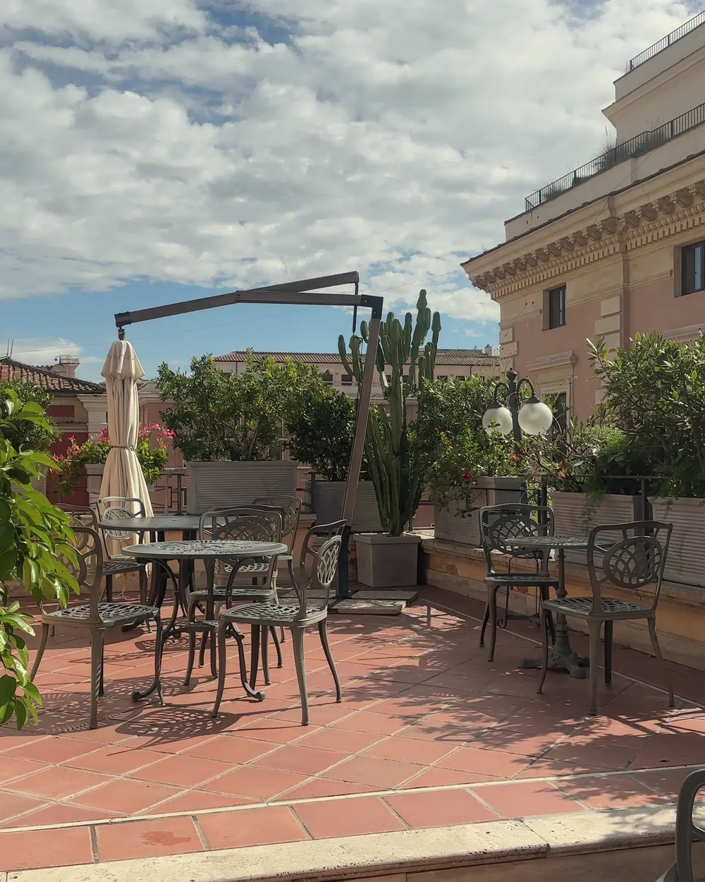 Wrought-iron tables and chairs on the rooftop terrace under a big blue sky with soft clouds