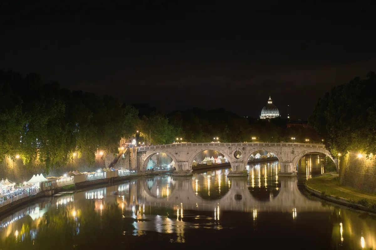 Ponte Sisto reflected in the Tiber at night, with the dome of St. Peter's lit in the distance