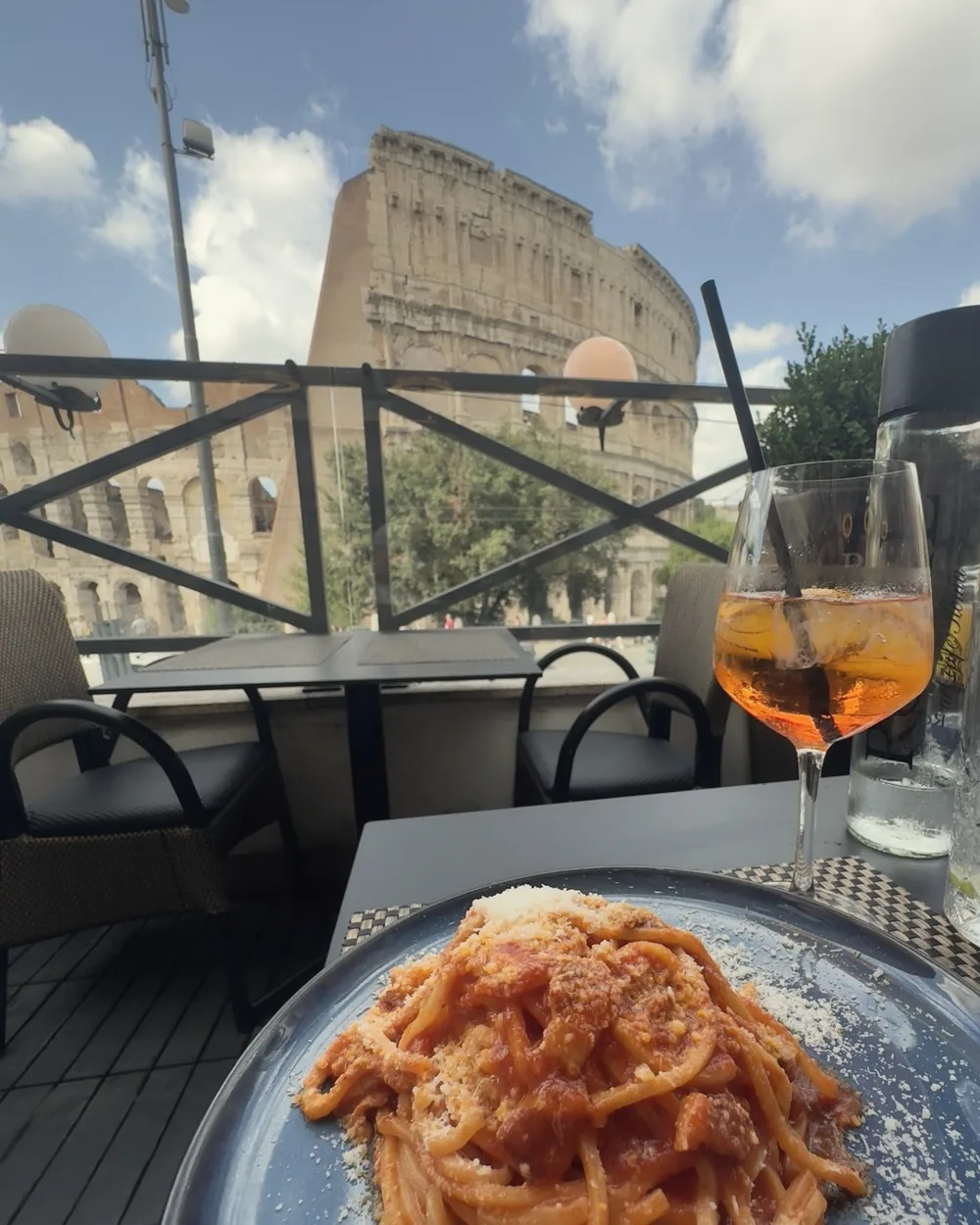 A plate of spaghetti and a spritz on a terrace table facing the Colosseum