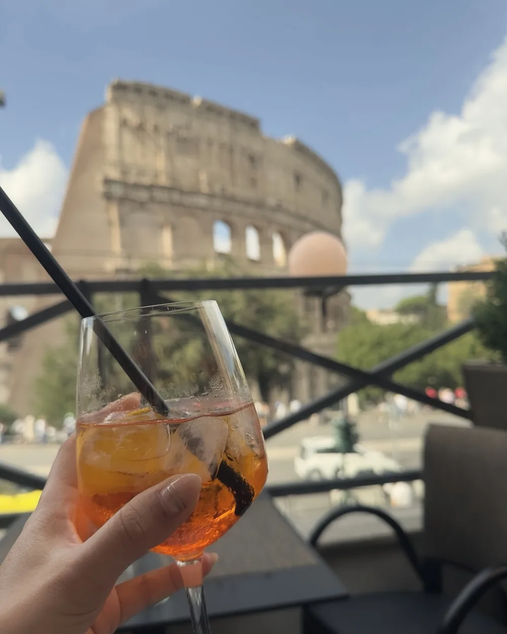 A hand raising an orange spritz on the Royal Art Café terrace, the Colosseum behind