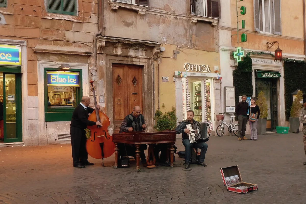 Street musicians playing double bass, cimbalom and accordion on the cobbles of Piazza di Santa Maria in Trastevere at dusk