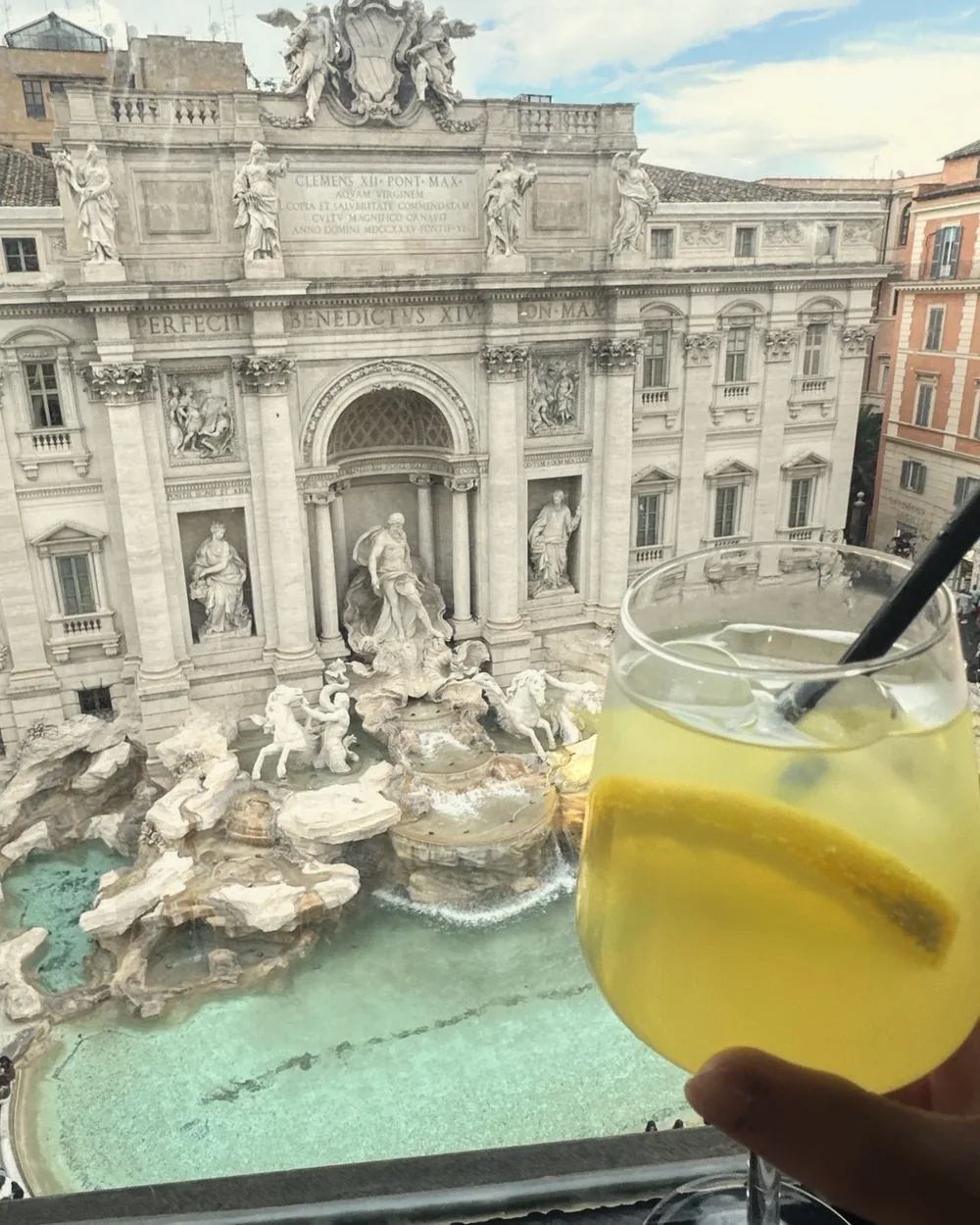 Looking straight down onto the Trevi Fountain's turquoise basin from a window, a spritz glass in the foreground
