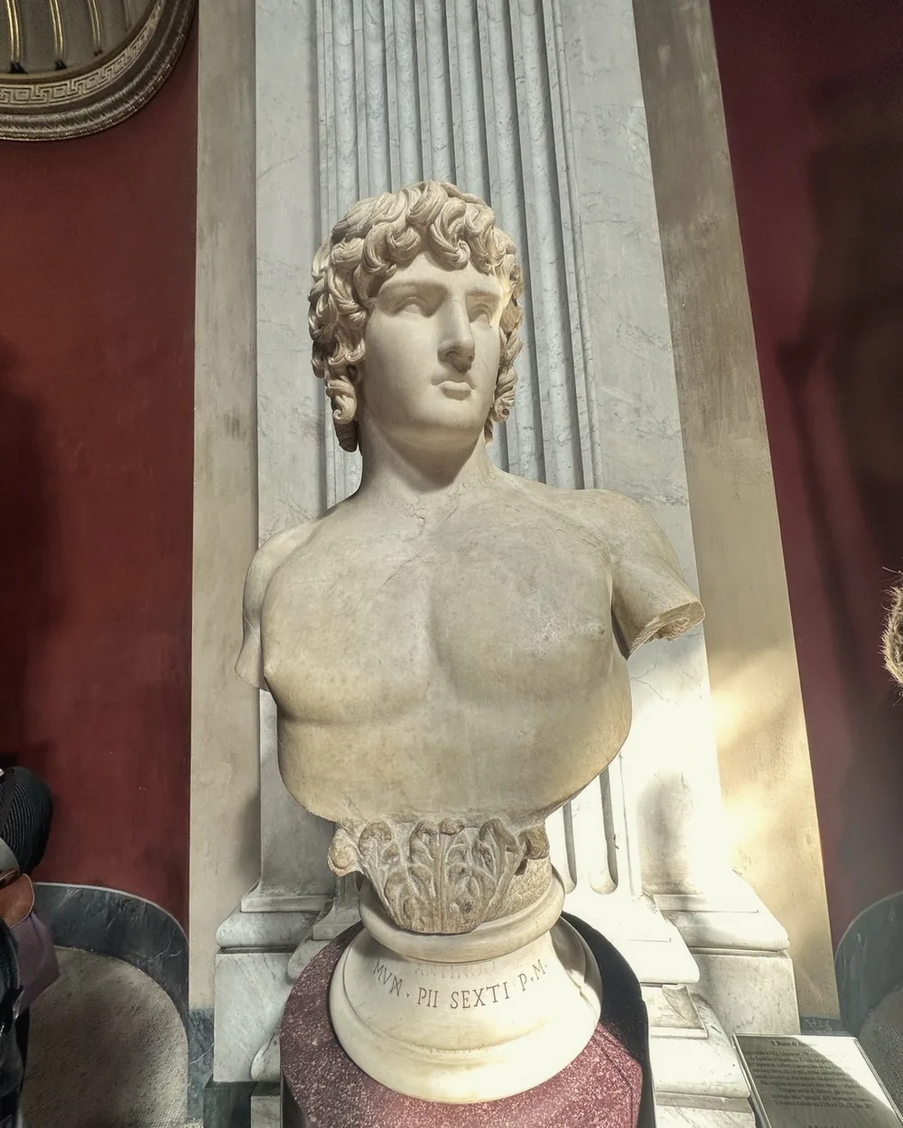 A classical marble bust against a deep red wall in the Vatican Museums