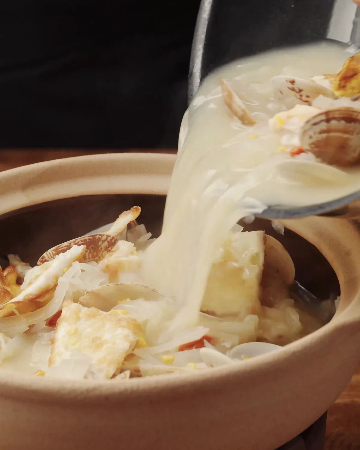 Creamy clam chowder being ladled into a terracotta bowl