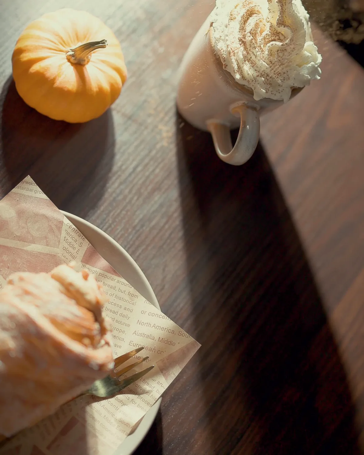 A latte with whipped foam, a mini pumpkin and a pastry on a warm wooden table