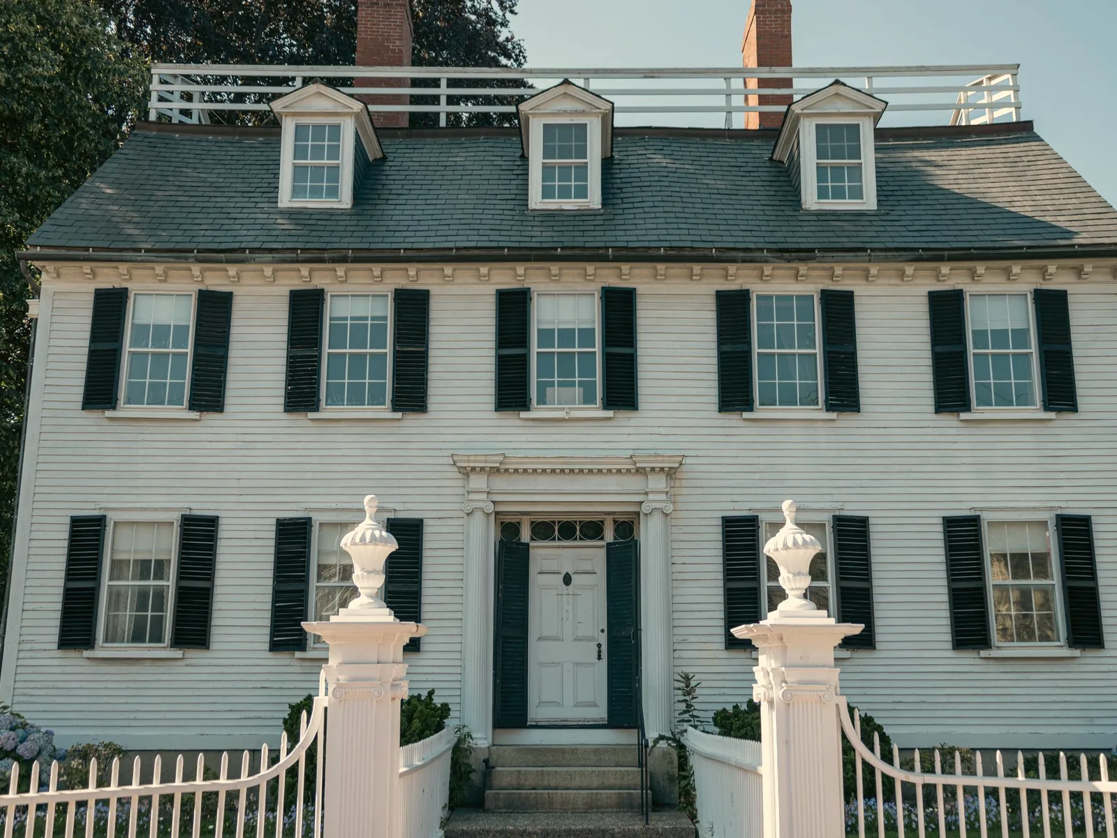 The white Georgian facade of the Ropes Mansion in Salem, with black shutters, a fanlit front door and carved urns on the gate posts