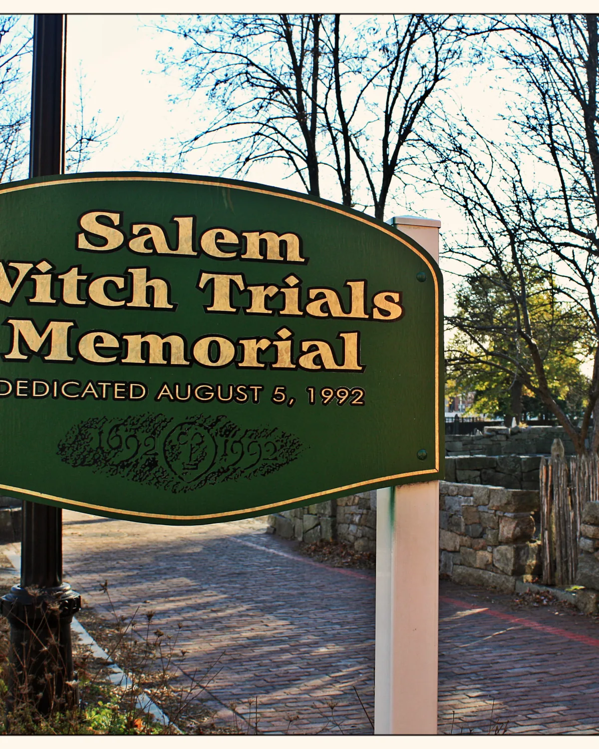 The green Salem Witch Trials Memorial sign beside a stone wall and autumn trees