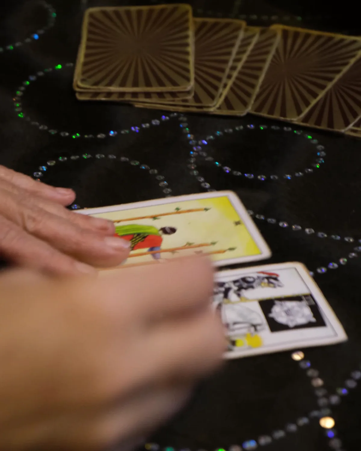 Hands laying tarot cards on a dark patterned cloth
