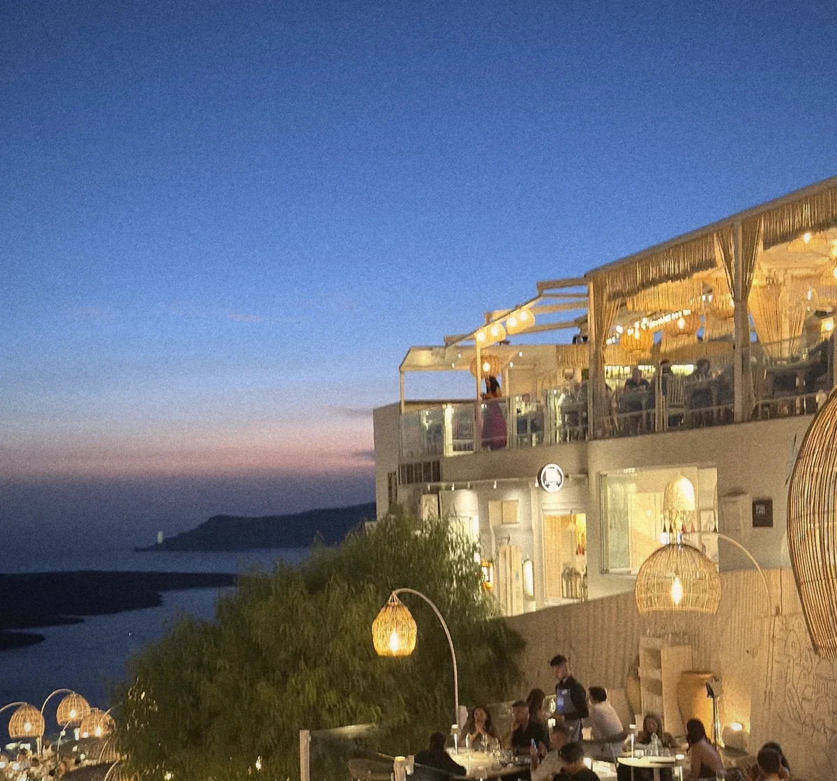 A lantern-lit restaurant terrace on the Santorini caldera at dusk