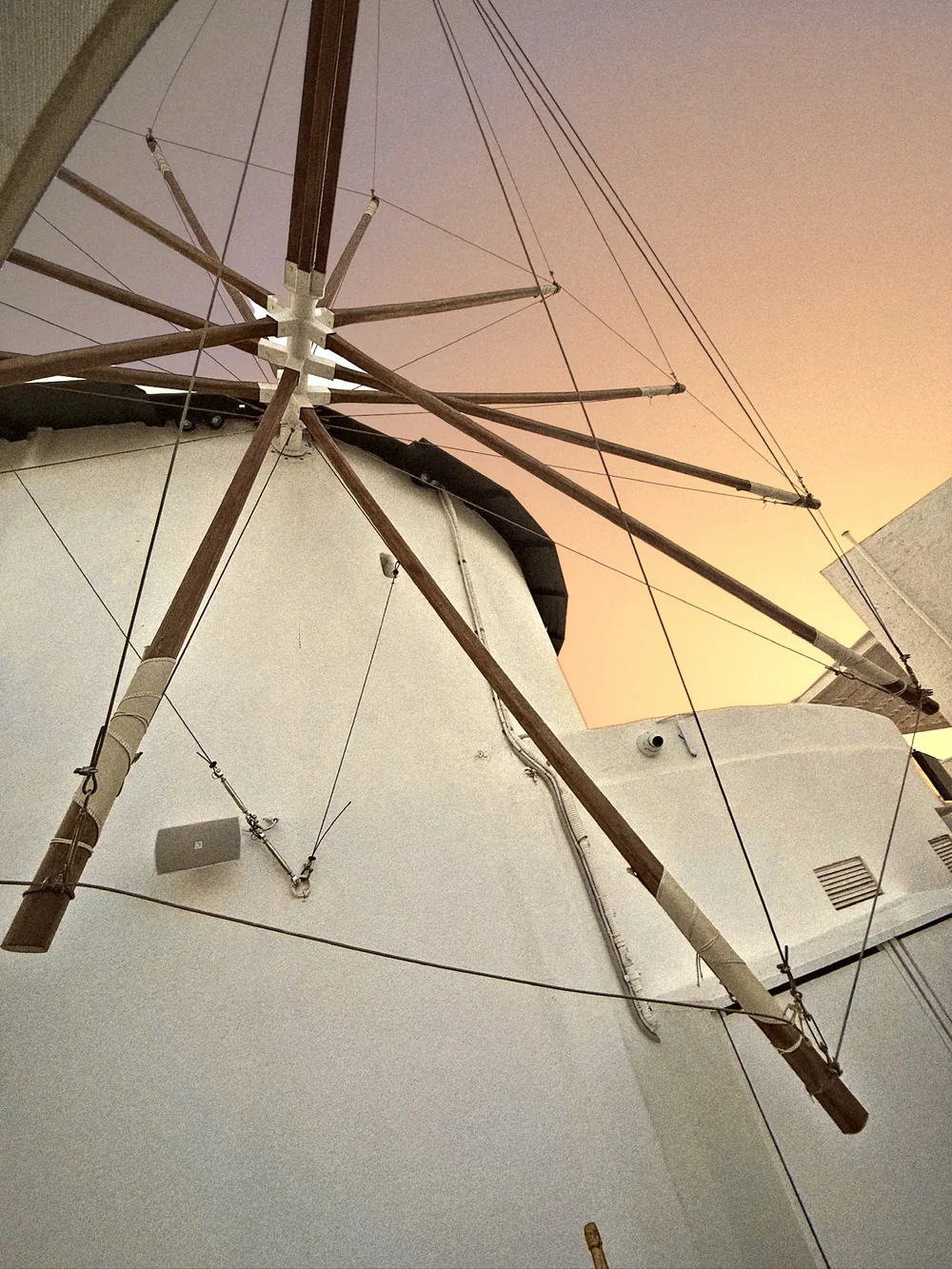 Looking up at the white Mylos windmill, its wooden sails and ropes lit by golden evening light in Firostefani, Santorini
