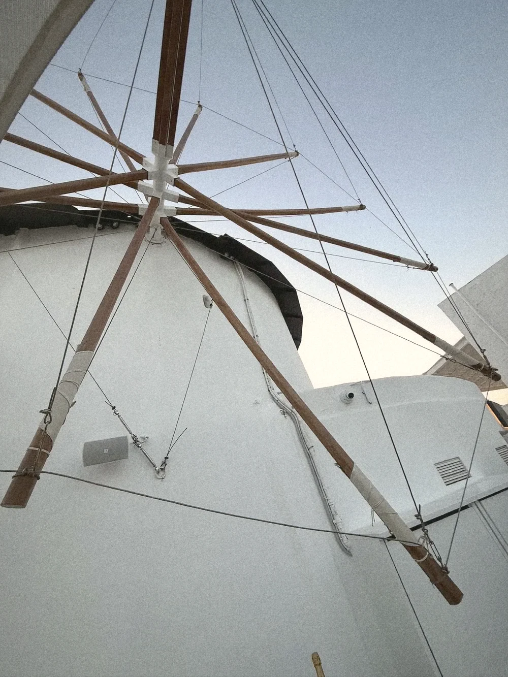 Looking up at the white Mylos windmill and its wooden sails against a pale blue sky