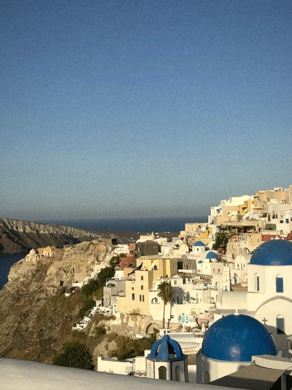 Oia's white and pastel houses cascading down the cliff above the caldera, with blue church domes in the foreground